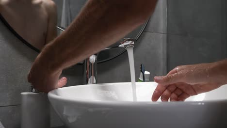 Man-is-washing-hands-with-soap-in-sink-to-prevent-coronavirus-Covid-19-infection.-Male-washes-hands-with-foam,-lathering-hands-and-rubbing-fingers-to-wash-skin.-Cleaning-and-preventing-germs-concept
