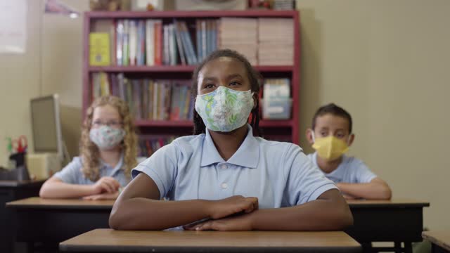 Grundschulkinder-tragen-Masken-im-Unterricht,-als-schwarzes-Mädchen-ihre-Hand-hebt