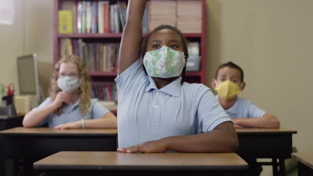 Junge-Schüler-tragen-Masken-und-hören-im-Unterricht-dann-schwarzeS-Mädchen-hebt-ihre-Hand
