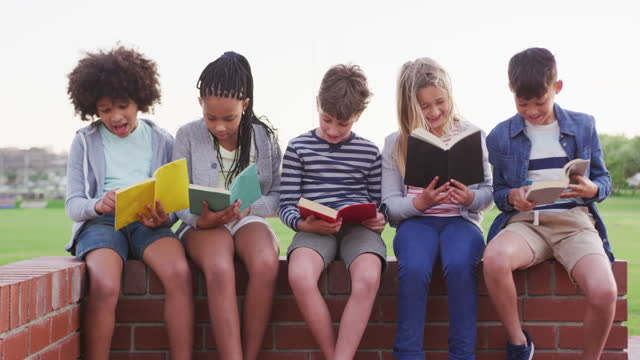 Gruppe-von-Kindern,-die-Bücher-lesen,-während-sie-auf-einer-Ziegelwand-sitzen