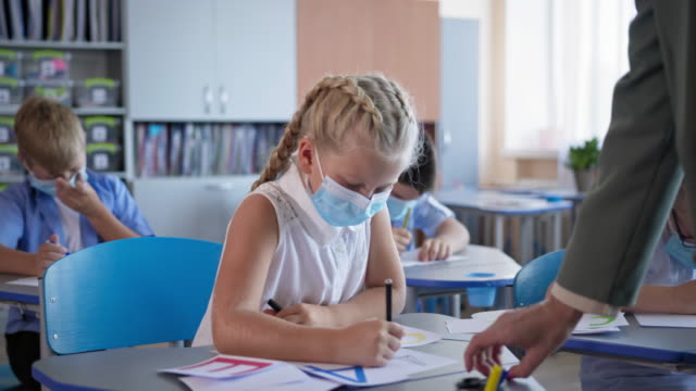pupils-in-medical-masks-doing-schoolwork-sitting-at-desk-in-the-classroom,-children-back-at-school-after-covid-19-quarantine-and-lockdown