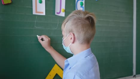 schoolboy-in-medical-mask-at-the-blackboard-writes-letters-with-chalk-in-classroom-at-school-after-quarantine-and-lockdown