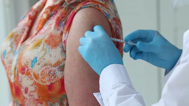 Close-up--woman-is-shoulder-and-a-doctor's-hands-in-medical-gloves-make-a-vaccine-against-the-Covid-19-coronavirus.-The-doctor-holds-a-syringe-and-gives-an-injection-to-a-senior-patient-wearing-.