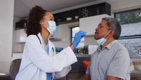 Gemischte-Rasse-Ärztin-trägt-Maske-tun-Tupfer-Test-auf-Senior-Mann-zu-Hause