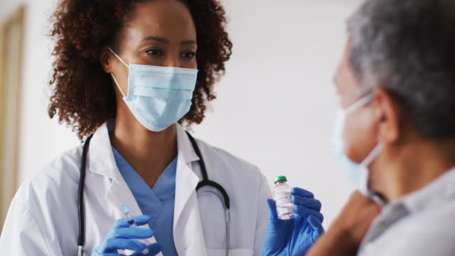 Gemischte-Rasse-Ärztin-trägt-Maske-geben-Impfung-für-Senior-Mann-zu-Hause