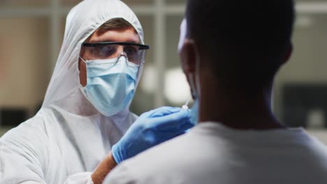 Caucasian-male-medical-worker-wearing-protective-clothing-taking-dna-swab-sample-from-patient-in-lab