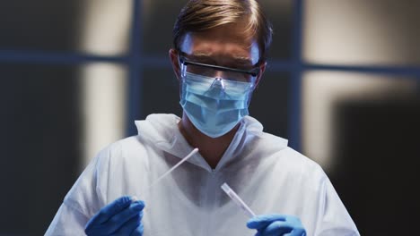 Caucasian-male-medical-worker-in-protective-clothing-and-face-mask-examining-patient-swab-test