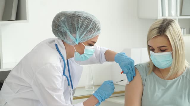 Krankenschwester-in-Handschuhen-und-Schutzmaske-impft-weibliche-Patientin-in-der-Klinik.-Arzt-injiziert-Impfstoff-gegen-Covid-19-in-die-Hand-von-Spritze.-Coronavirus
