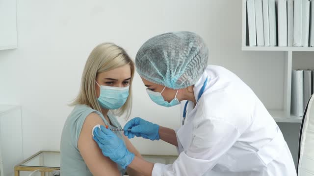 Krankenschwester-in-Handschuhen-impft-weibliche-Patientin-in-Maske-im-Krankenhaus.-Arzt-injiziert-Medikamente-aus-Spritze-in-die-Hand.-Coronavirus-Impfstoff
