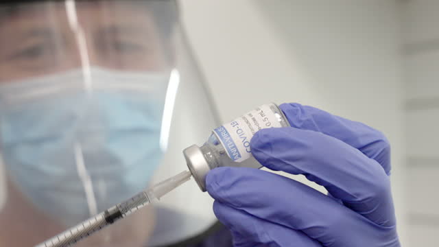 Nahaufnahme-eines-Männchens-in-ppe-füllt-eine-Spritze-mit-Covid-19-Impfstoff-aus-einer-Durchstechflasche