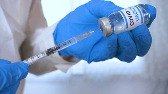 Arzthände-mit-blauen-chirurgischen-Handschuhen-mit-Spritze-und-COVID-19-Impfstoff.-COVID-19-Impfstoffkonzept.-Gesundheits--und-medizinisches-Konzept.-Selektiver-Fokus,-Spritzen--und-Impfstoffdosis-ausnächster-Nähe.-Makro-4K-Video.