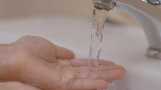 Slow-Motion.-Closeup-of-Human-Hand-Under-Stream-of-Pure-Water-From-Tap.-Child-Palm-Under-Stream-of-Water-Slow-Motion.-Little-Girl-in-Bathroom-at-Home-Checking-Temperature-Touching-Running-Water.