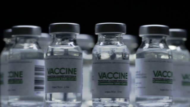 Impfstoffflaschen-zur-CoVID-19-Coronaviruskur-werden-im-Forschungslabor-schnell-gedreht.-Impfung,-Injektion,-klinische-Studie-während-der-Pandemie.-Fläschchen,-Fläschchen-drehen-sich-im-Uhrzeigersinn.-Breites-Makro-im-Dunkeln
