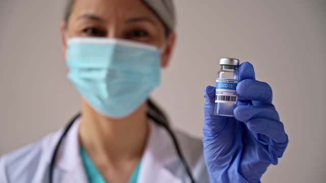 Una-mujer-desenfocada,-una-trabajadora-médica,-que-lleva-máscara-médica,-sostiene-una-ampolla-con-una-vacuna-contra-el-coronavirus,-covid19.-Concepto-de-vacunación-y-atención-sanitaria