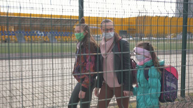 A-Mother-and-two-daughters-in-a-protective-anti-virus-mask-walk-along-the-street-in-an-isolated-area.
