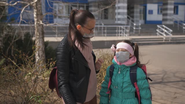 A-Mother-in-a-protective-mask-is-waiting-for-a-little-daughter,-first-grader-from-school-after-school.-Schoolgirl-first-grader-in-protective-mask-runs-up-to-mom
