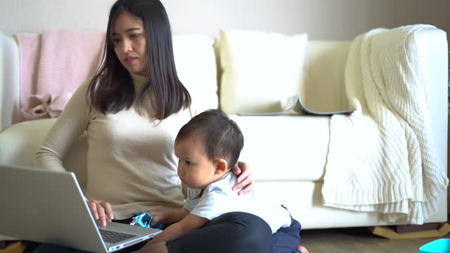 Yong-Mutter-arbeitet-mit-Laptop-zu-Hause-und-ihr-Sohn-spielt-neben-ihr.