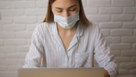 A-girl-in-a-striped-pejama-against-a-brick-wall-wearing-a-medical-mask.-Works-remotely.-Close-up.-Selective-focus.-front-view
