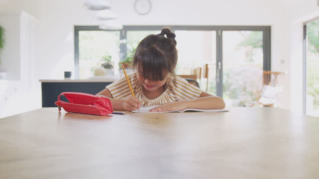 Junge-asiatische-Mädchen-zu-Hause-Schulbildung-arbeiten-am-Tisch-in-Küche-Schreiben-in-Buch-während-Lockdown