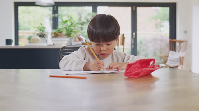 Junge-asiatische-Junge-ZuHause-Schularbeiten-am-Tisch-in-Küche-Schreiben-in-Buch-während-Lockdown