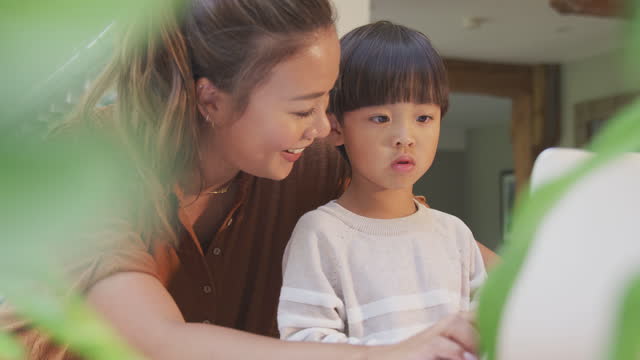 Asiatische-Mutter-hilft-zu-Hause-Schulbildung-Sohn-arbeiten-am-Tisch-in-Küche-auf-Laptop