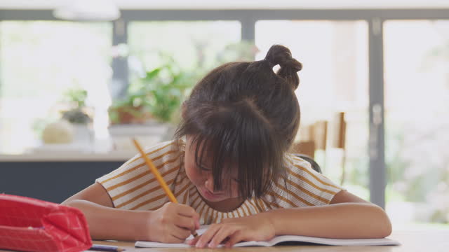 Junge-asiatische-Mädchen-zu-Hause-Schulbildung-arbeiten-am-Tisch-in-Küche-Schreiben-in-Buch-während-Lockdown