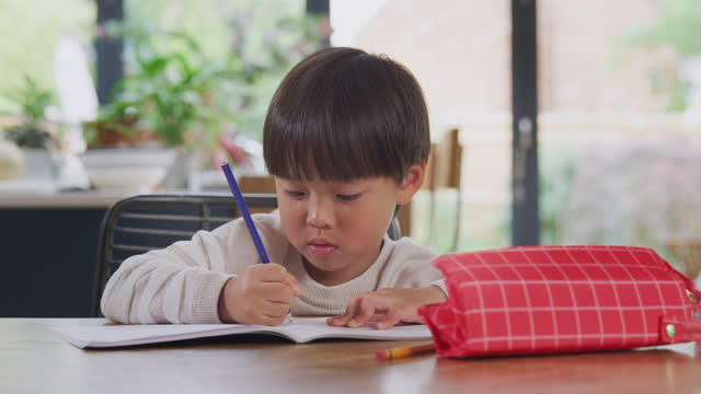 Junge-asiatische-Junge-ZuHause-Schularbeiten-am-Tisch-in-Küche-Schreiben-in-Buch-während-Lockdown