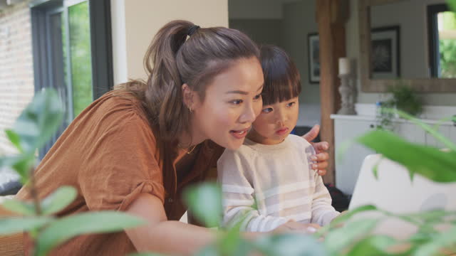 Madre-asiática-ayudando-a-su-hijo-de-la-escuela-en-casa-trabajando-en-la-mesa-en-la-cocina-en-el-ordenador-portátil