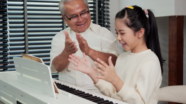 Grandfather-looking-granddaughter-playing-piano-at-living-room.-She-was-showing-play-piano-to-Grandfather-with-confident.