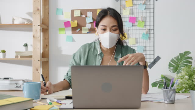 Asia-businesswoman-wearing-medical-face-mask-using-laptop-talk-to-colleagues-about-plan-in-video-call-while-working-from-home-at-living-room.