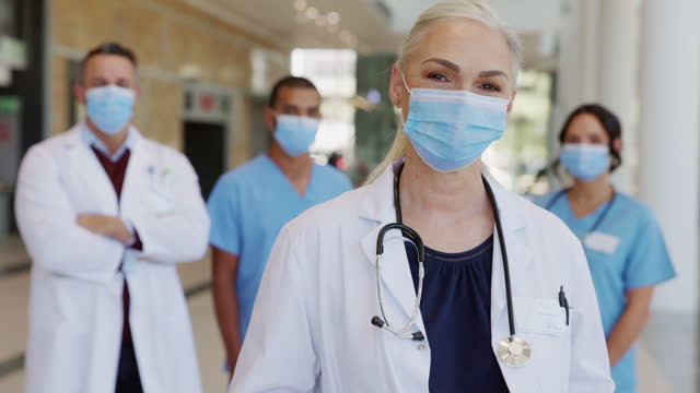 Satisfied-senior-doctor-wearing-face-mask-with-team-in-background