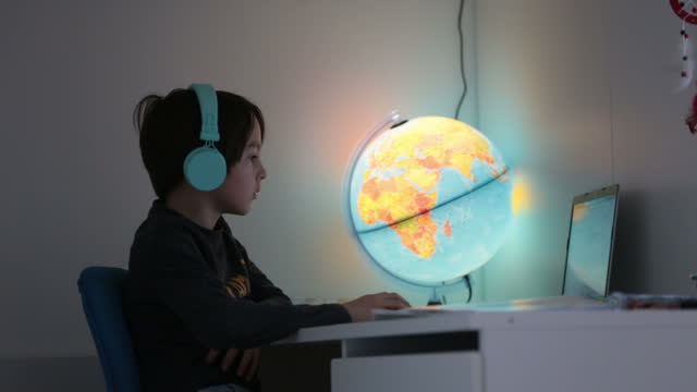 Hermoso-niño-con-auriculares-usando-computadora-portátil-mientras-estudia-en-el-escritorio-en-casa-durante-el-coronavirus