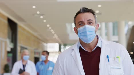 Reife-Arzt-mit-Gesichtsmaske-zu-Fuß-im-Krankenhaus-Korridor