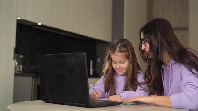 Distance-learning-concept.-girl-schoolgirl-with-her-mom-learns-online-using-a-laptop,-making-notes-in-a-notebook.-Online-video-course,