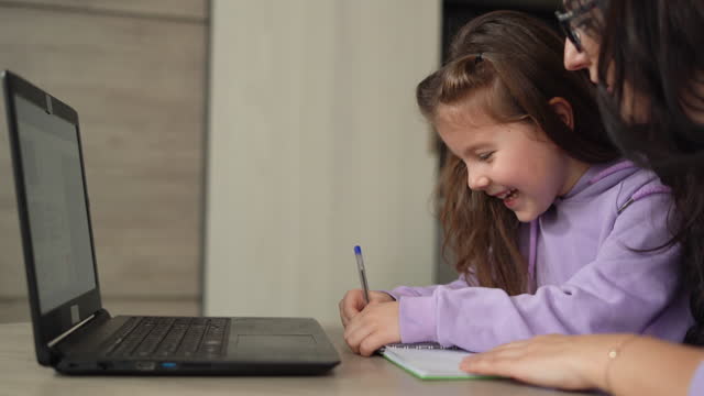 Distance-learning-concept.-girl-schoolgirl-with-her-mom-learns-online-using-a-laptop,-making-notes-in-a-notebook.-Online-video-course,