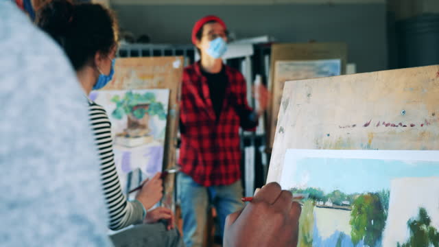 Schüler-malen-während-des-Kunstunterrichts-mit-einem-Lehrer-in-einer-Gesichtsmaske