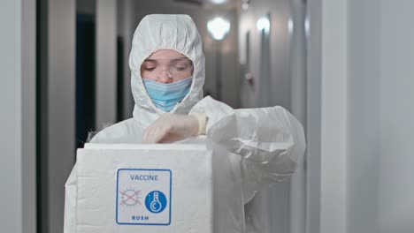 Mediziner-in-Schutzkostüm,-der-Coronavirus-Impfstoff-demonstriert.-Zoom-in-der-schweren-Ärztin-in-Schutzuniform-mit-Maske-und-Schutzbrille,-die-Flasche-mit-Covid-19-Impfstoff-aus-Stickstoff-Gefrierbox-nimmt-und-vor-der-Kamera-in-langsam