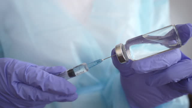 Doctor's-hands-in-medical-gloves-filling-syringe-with-vaccine-from-glass-bottle