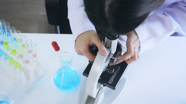 Woman-looking-through-microscope-in-lab