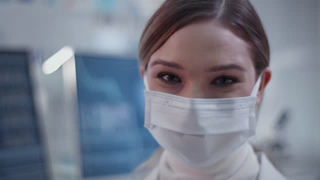 Ärztin-trägt-Maske-im-Labor.-Zufrieden-mit-ihrer-Arbeit.-Lächelnd-in-eine-Kamera