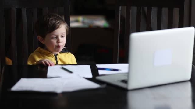 Kleiner-Junge-sitzt-am-Tisch-mit-Laptop-und-Dokumente-für-den-Unterricht-zu-Hause