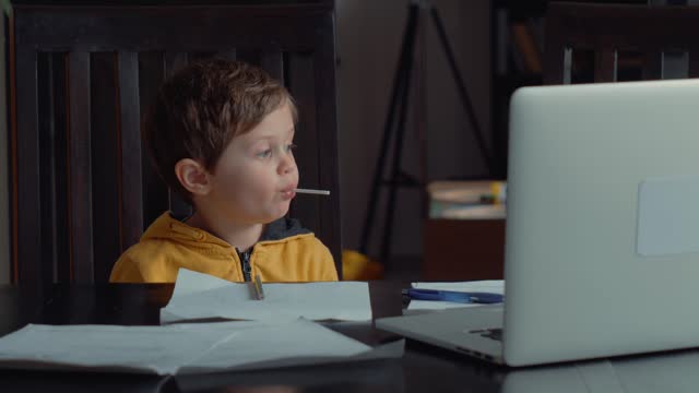 Kleiner-Junge-sitzt-am-Tisch-mit-Laptop-und-Dokumente-für-den-Unterricht-zu-Hause