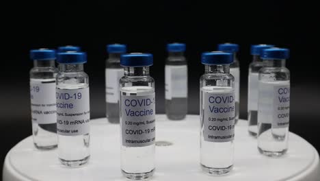 Glasfläschchen-mit-Covid-19-Vaccine-auf-rotierendem-Display-isoliert-auf-schwarzem-Hintergrund.