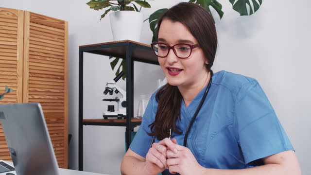 Telemedizin-Konzept.-Glückliche-junge-medizinische-Fachfrau-in-blauen-Peelings-berät-Patient-online-über-Laptop-Webcam