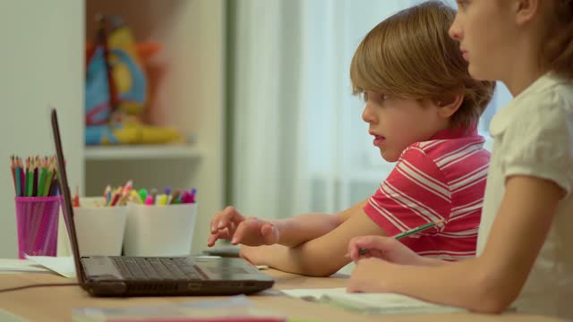 Online-Fernunterricht-von-Kindern-zu-Hause-mit-einem-Laptop.-Schwester-und-Bruder-schreiben-in-Notizbücher.-Coronavirus-Covid19-Ausbruch.