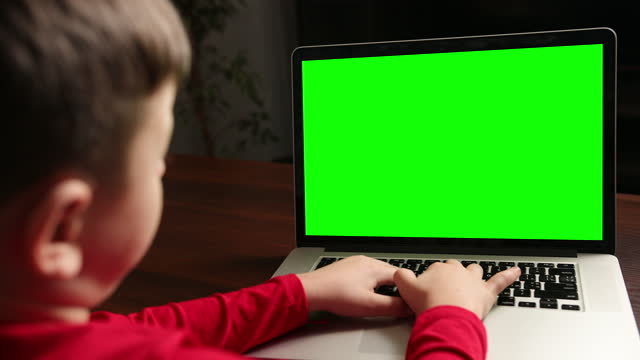 Vista-desde-el-niño-de-atrás-sentado-en-la-mesa-escribiendo-en-el-ordenador-portátil-con-clave-de-croma-verde