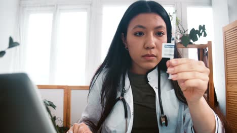Acercar-a-la-mujer-doctora-multiétnica-profesional-en-bata-de-laboratorio-que-busca-una-nueva-cura-de-jeringa-vacunal,-comprobando-con-el-ordenador-portátil.