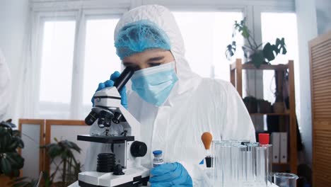 Experto-en-laboratorio-químico-en-el-trabajo.-Joven-científico-farmacéutico-enfocado-en-traje-de-protección-utilizando-la-vacuna-de-pruebas-de-microscopio.