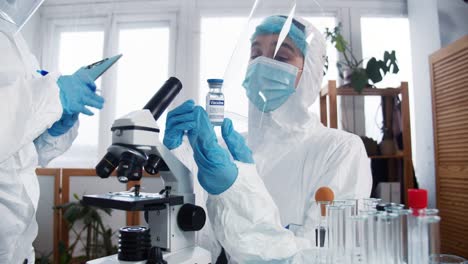 Creating-new-coronavirus-vaccine.-Professional-doctor,-scientist-woman-in-protection-suit-holds-cure-flask-at-clinic-lab