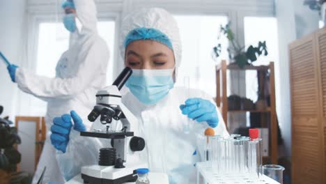 Científico-de-laboratorio-químico-en-el-trabajo.-Joven-experto-farmacéutico-enfocado-en-traje-de-protección-utilizando-la-vacuna-de-prueba-de-microscopio.